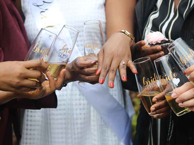 Women holding drinking glasses and looking at a ring on someone's hand