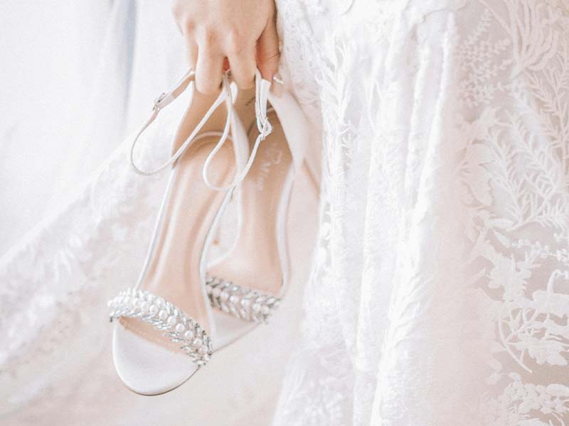 Woman in wedding dress carrying sandals