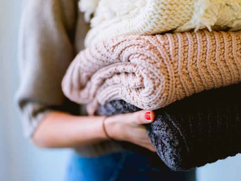 Woman holding pile of sweaters