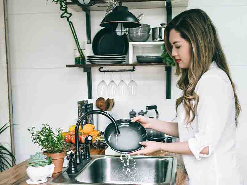 Woman washing pot in kitchen sink