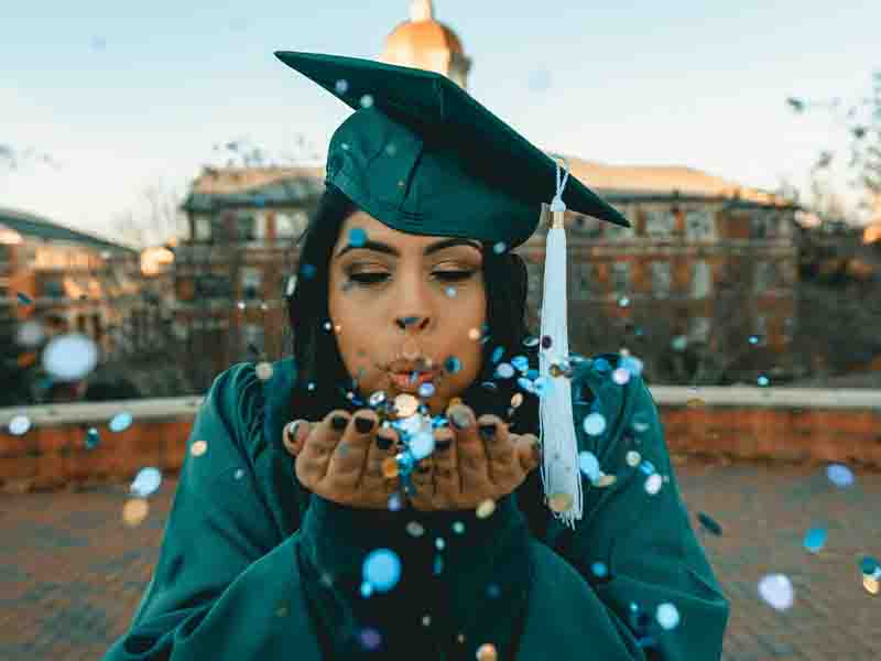 Woman in graduation gown and hat blowing sequins into air