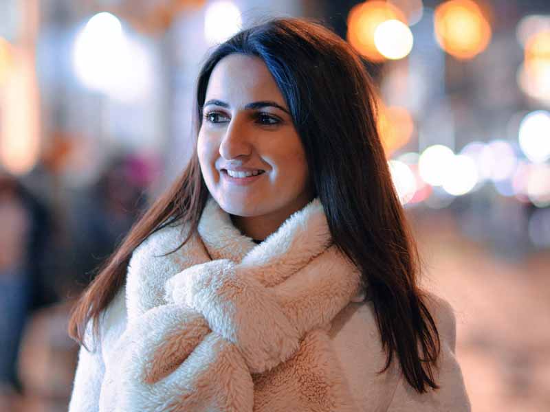 Woman with white scarf and coat and lights in background