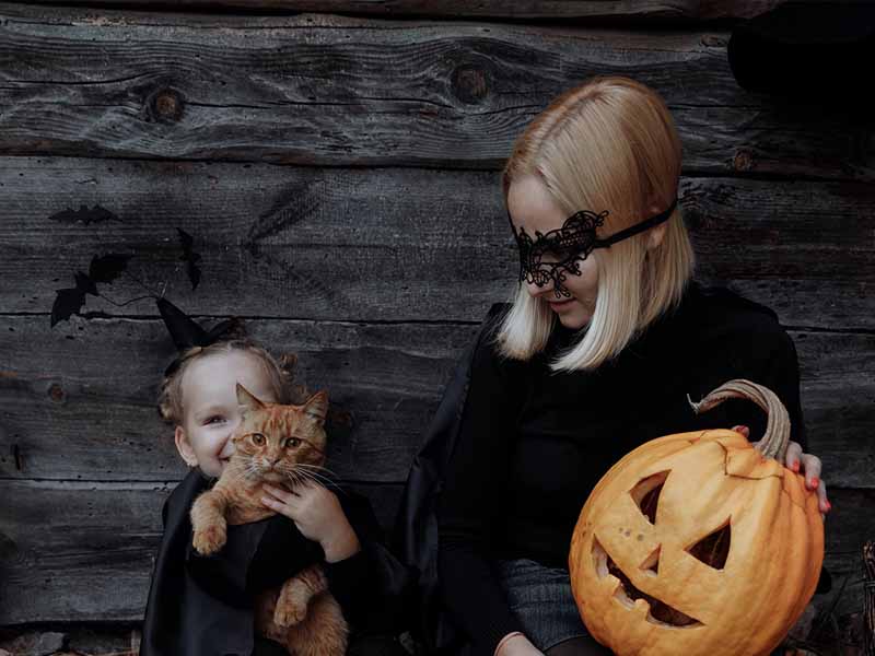 Mother and daughter in matching halloween costumes, holding a jackolantern