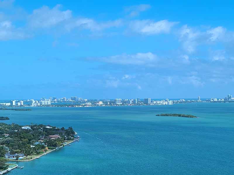 A shot of Biscayne Bay in Florida, from above. Blue sunny sky and blue water with a small white boat sailing.
