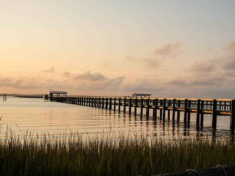 Chesapeake Bay bridge shot at sunset with orange and yellow sky reflecting on water.